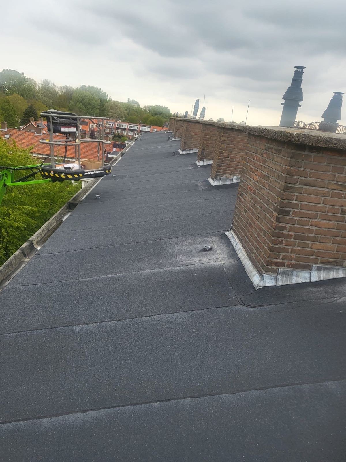 Schoorsteen met loodwerk op een plat dak, bereikbaar met een hoogwerker