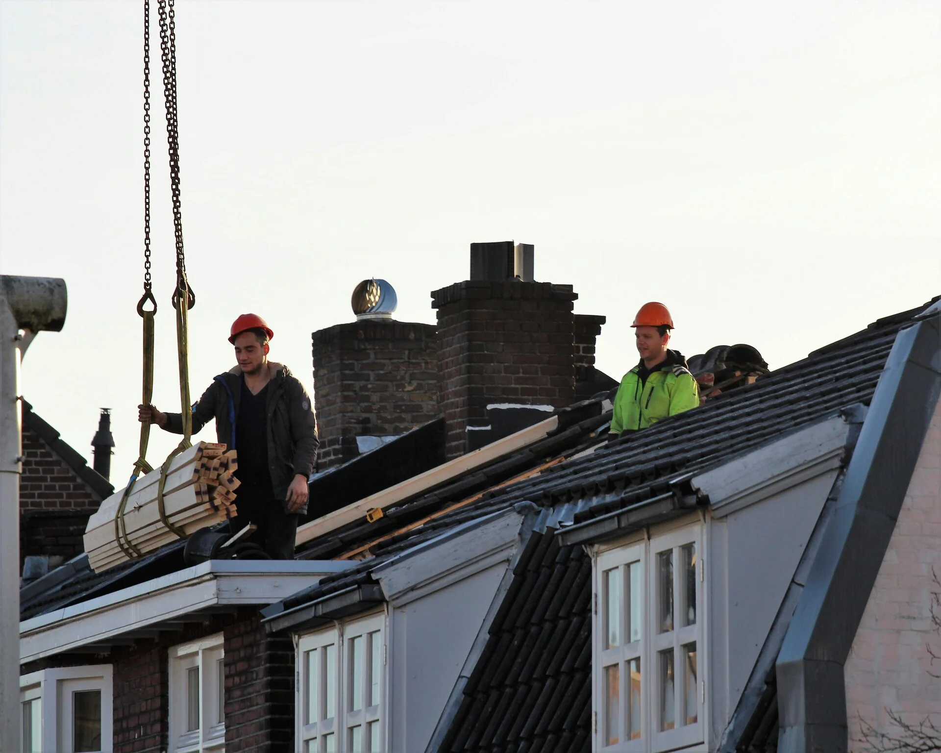 Dakdekkers hijsen hout omhoog voor werkzaamheden aan een dak met dakkapellen